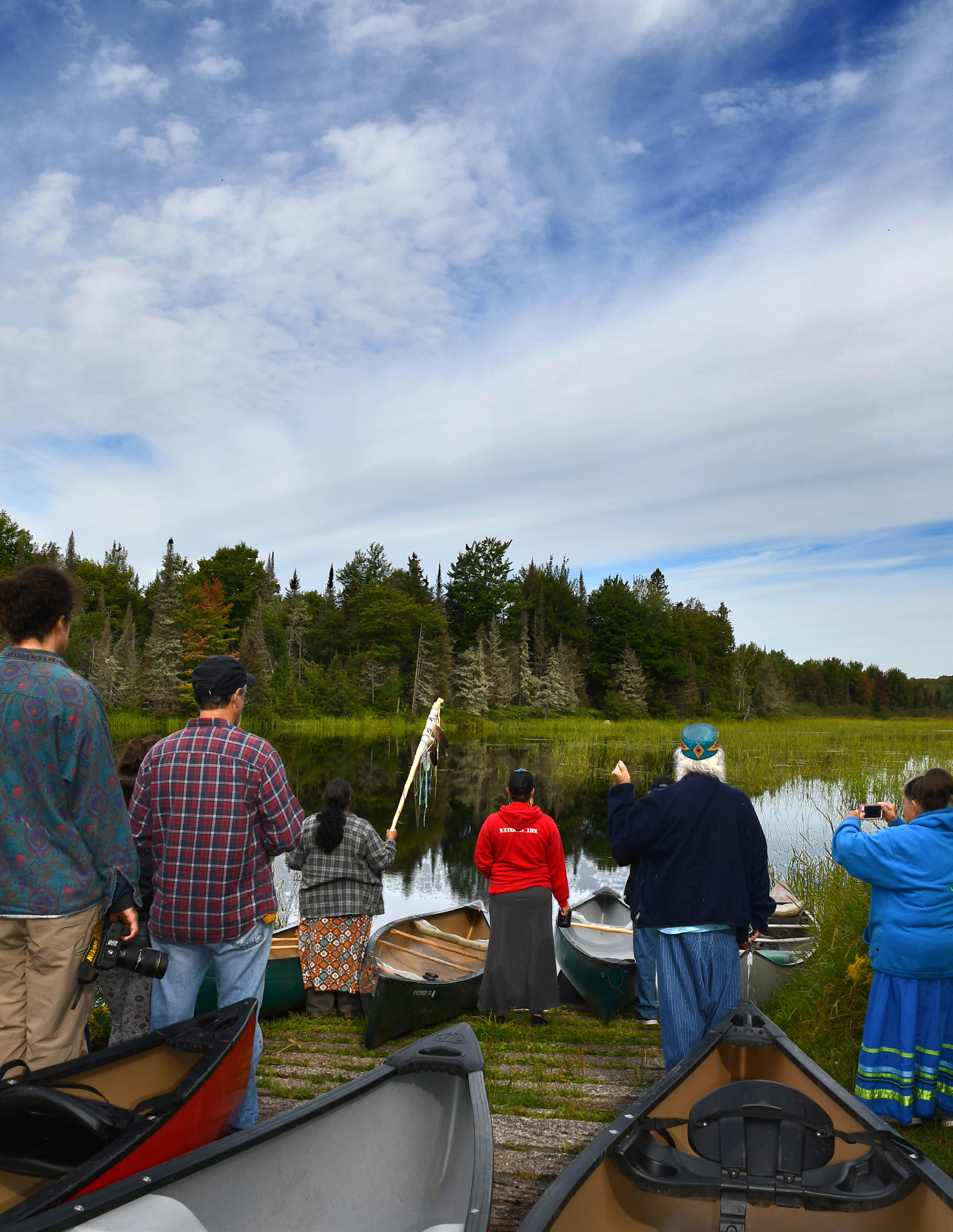 Community members standing at the shore with canoes, looking out over a wild rice lake in Michigan