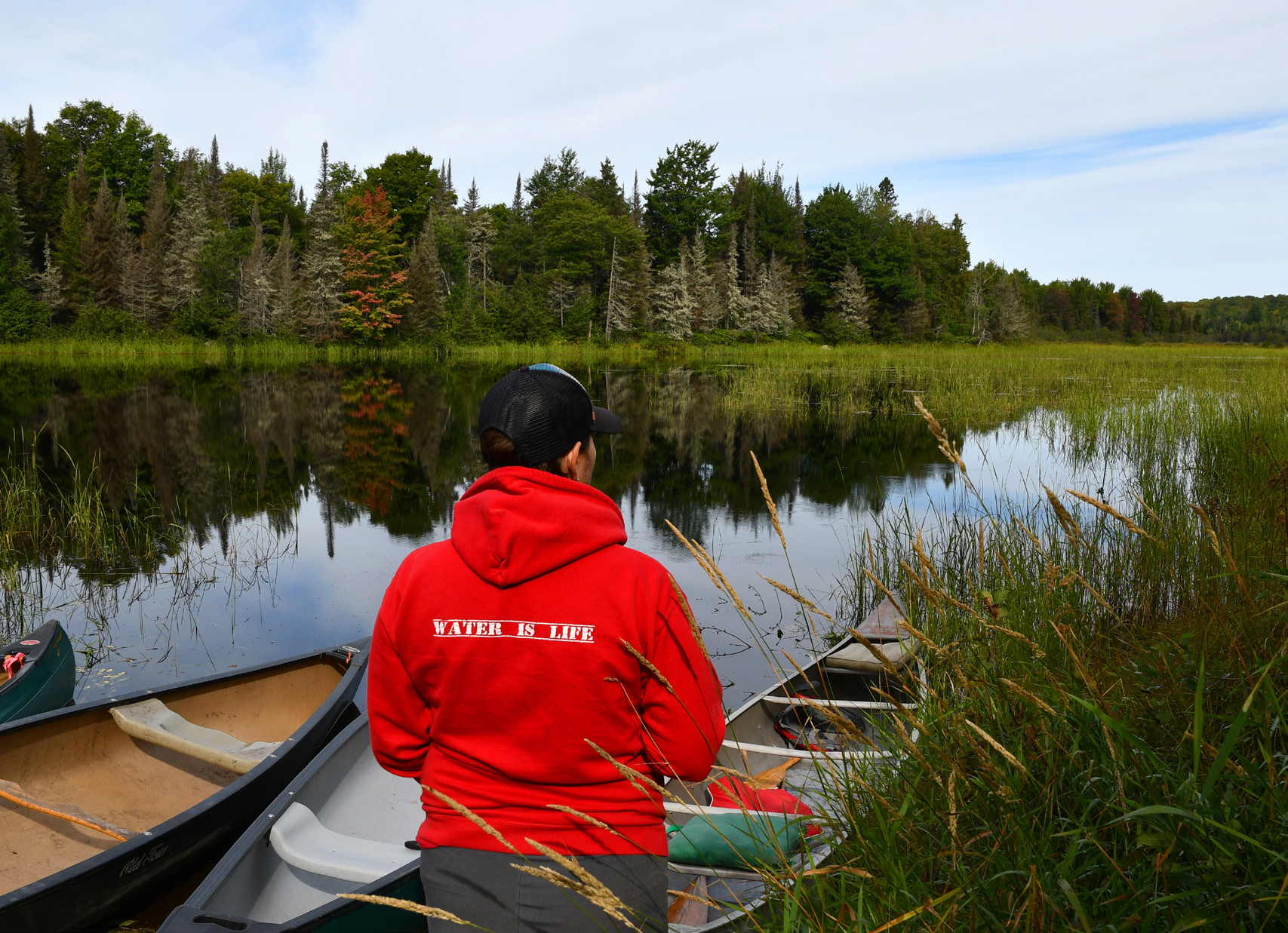 Person sitting in a canoe among Manoomin beds on a calm Michigan lake